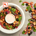 Plated salad with chicken, vegetables, and a dipping sauce on a wooden surface.