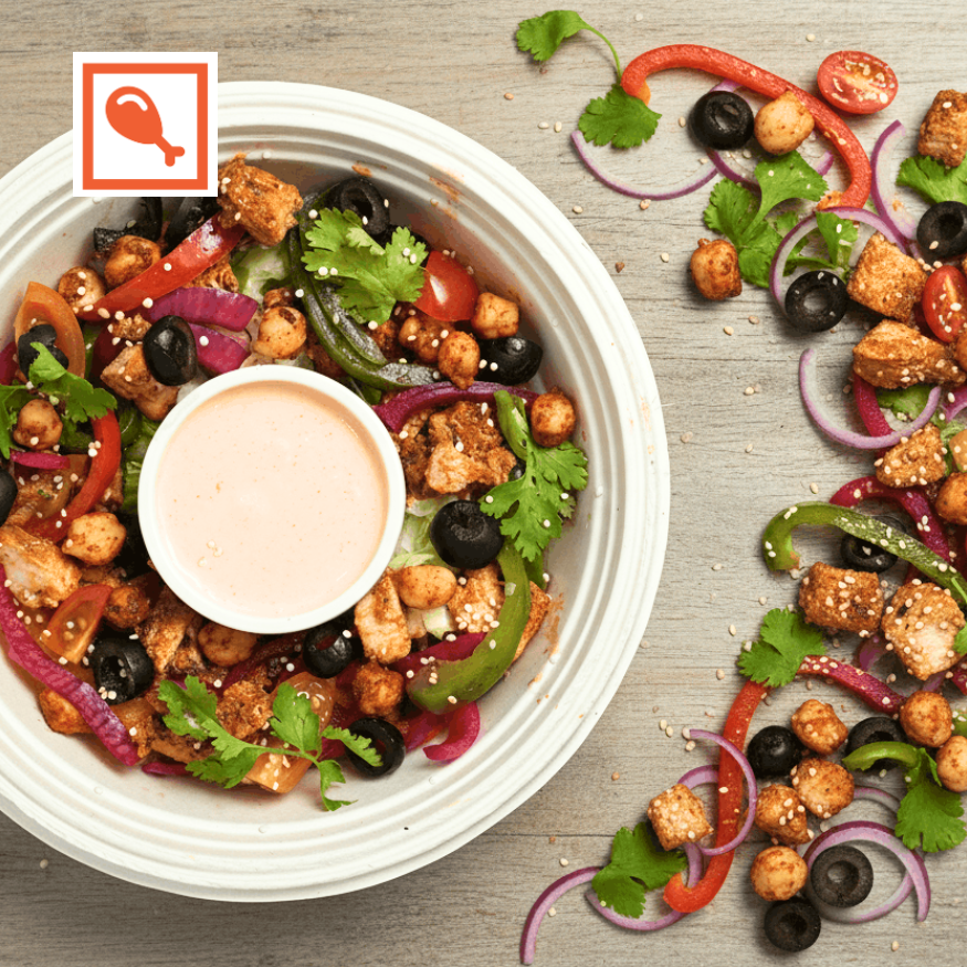 Plated salad with chicken, vegetables, and a dipping sauce on a wooden surface.